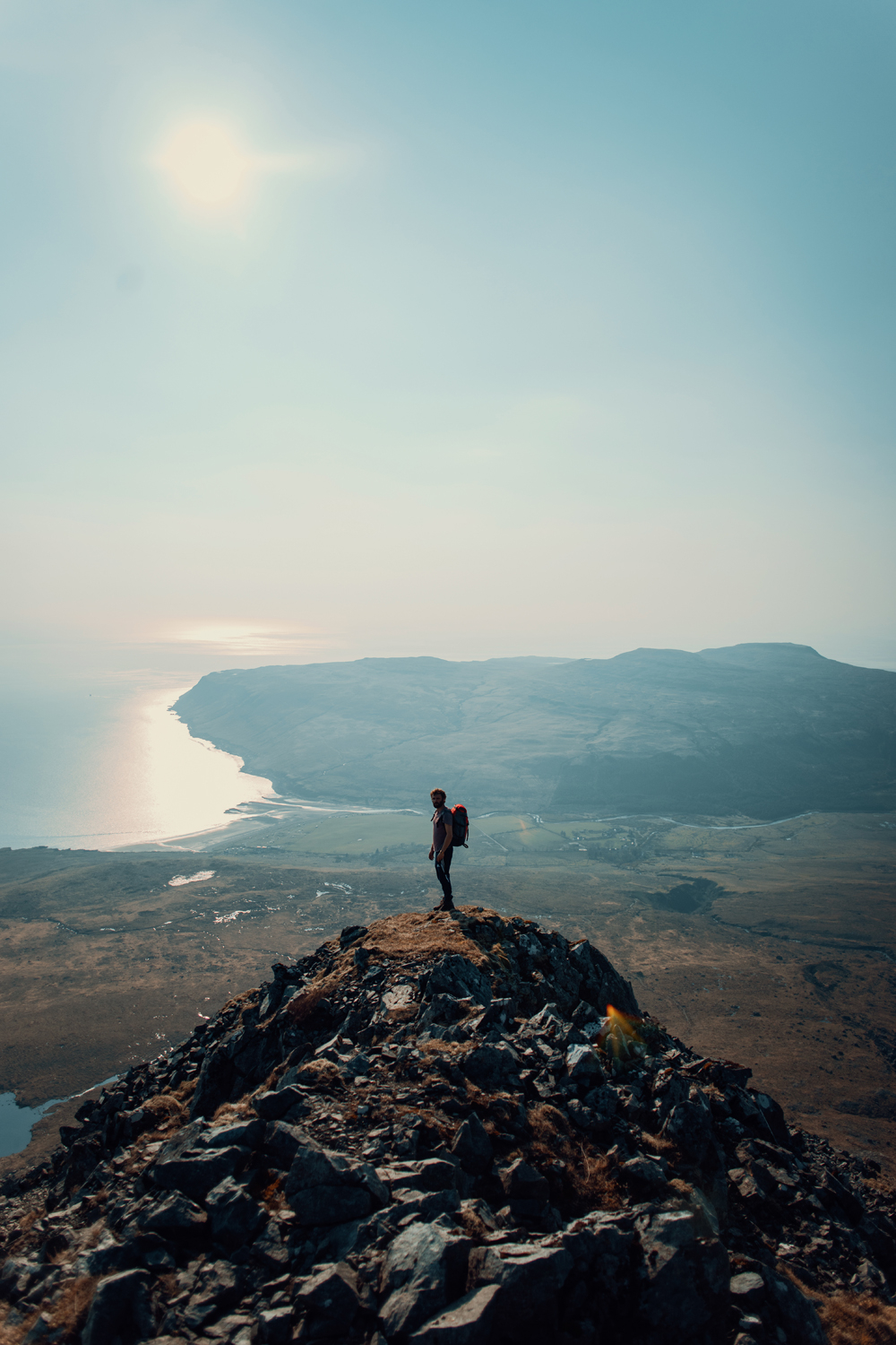 A hiker standing on a rocky mountain peak overlooking the sea, captured by David Velez photography.