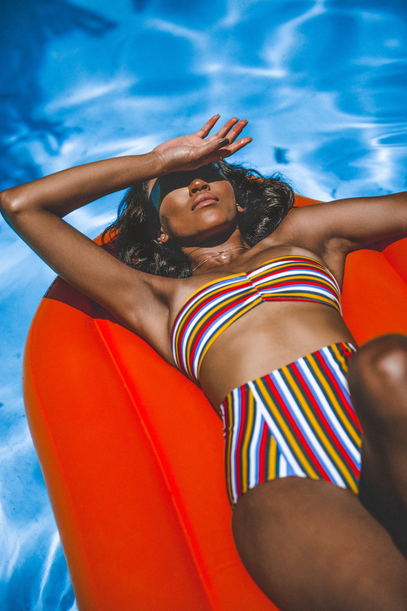A woman in a striped swimsuit floating on an orange raft in a blue pool, showing how to avoid overediting photos using the HSL panel Lightroom features.