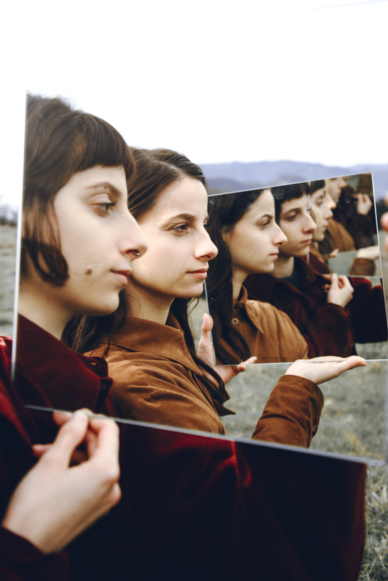 Conceptual portraiture showcasing creative visual storytelling with layered mirror reflections in an open landscape.