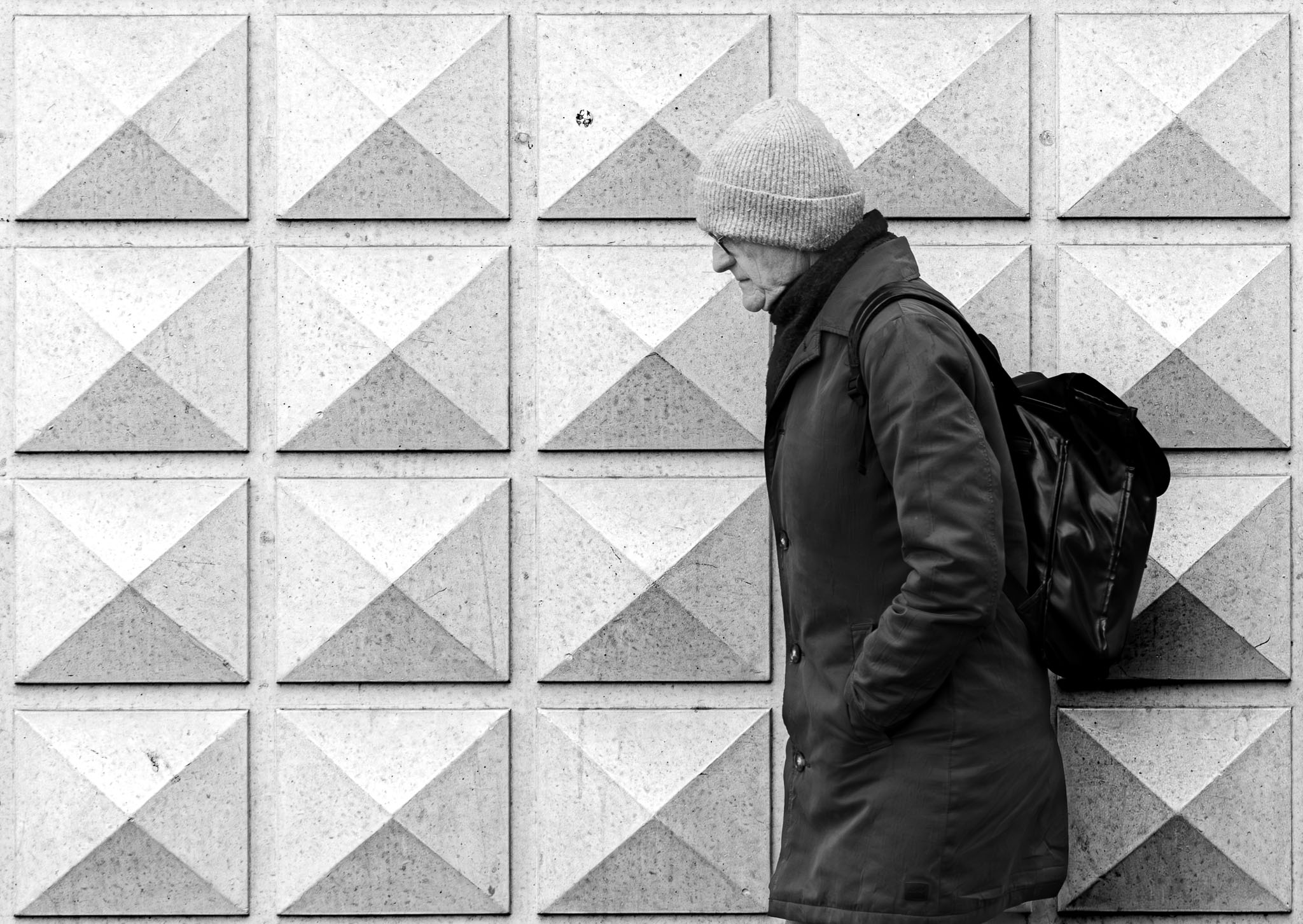 Elderly man in a knitted cap walking past a wall of concrete pyramids in Den Bosch