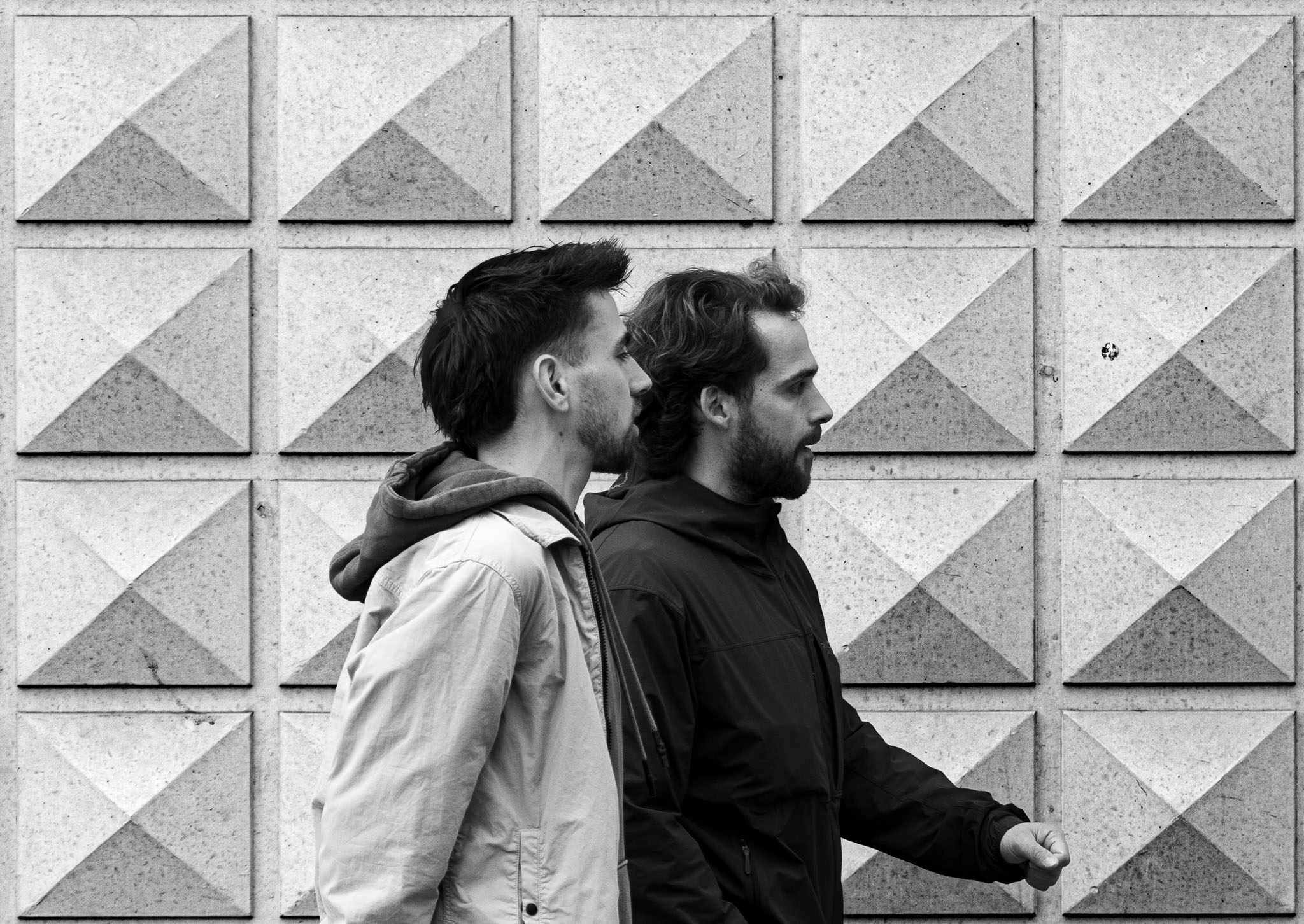Street photography composition of two men passing a wall of concrete pyramids in Den Bosch