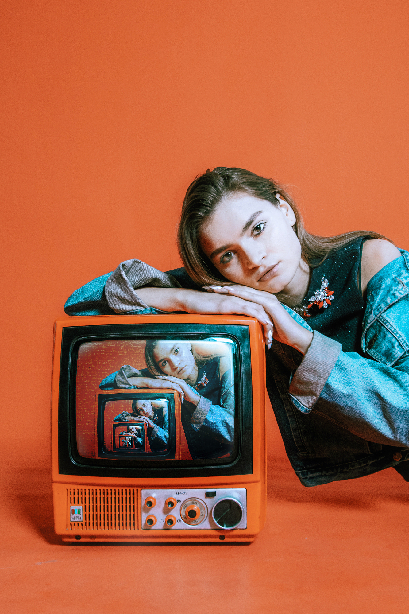 Young woman in a blue denim jacket leaning on a vintage orange television set, illustrating complementary color contrast photography.