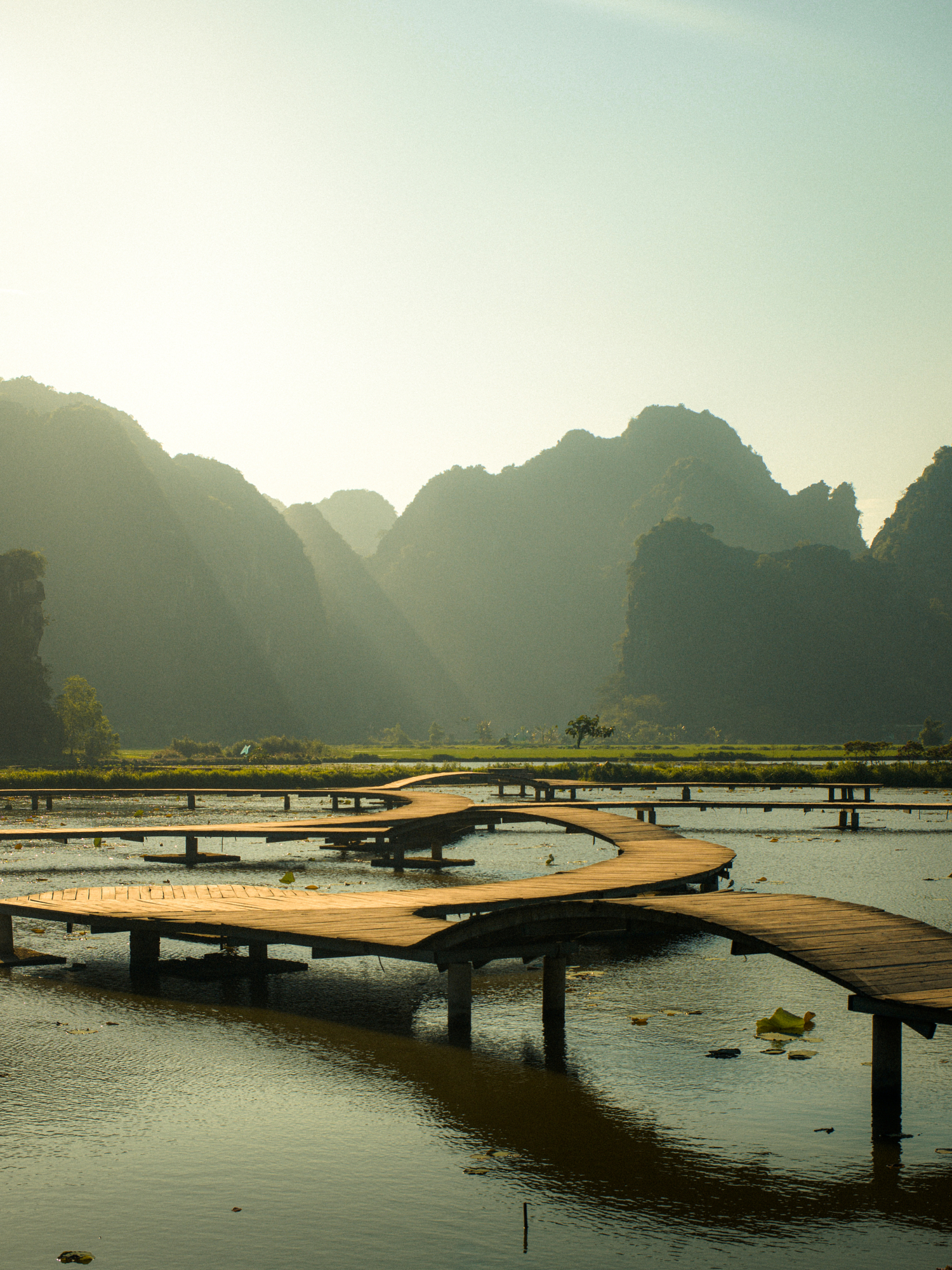 Nostalgic travel photography of a winding wooden boardwalk across a misty karst lagoon by Žak Mogel