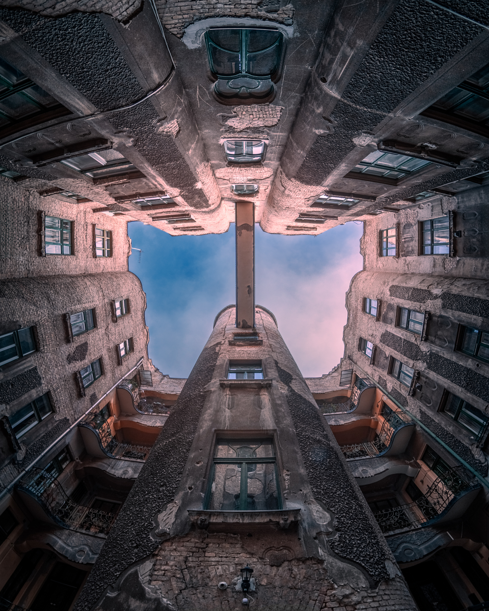 Look-up view of an ornate tenement courtyard opening onto a pink dawn sky