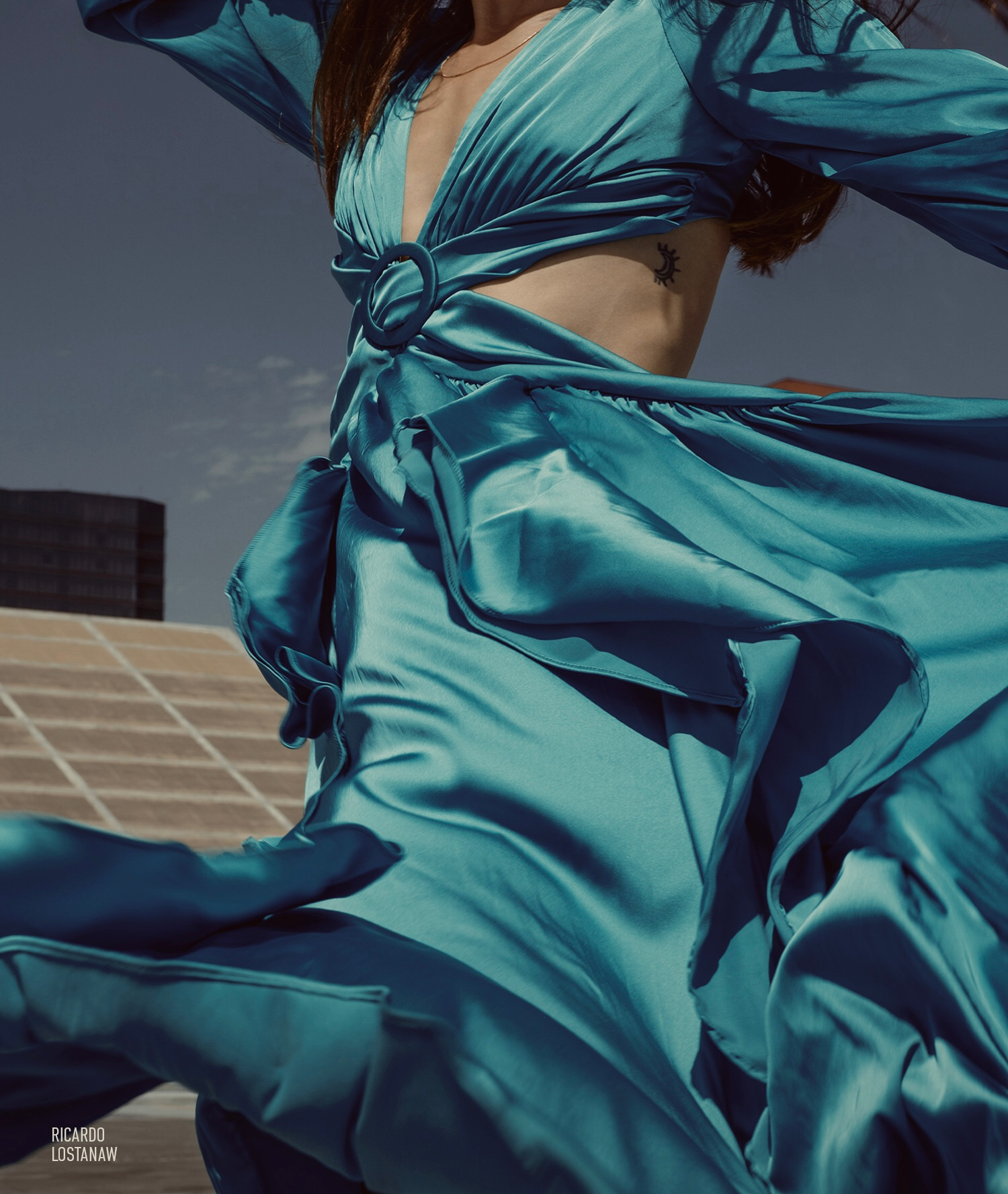 Teal satin dress caught mid-motion on a rooftop against a clear sky