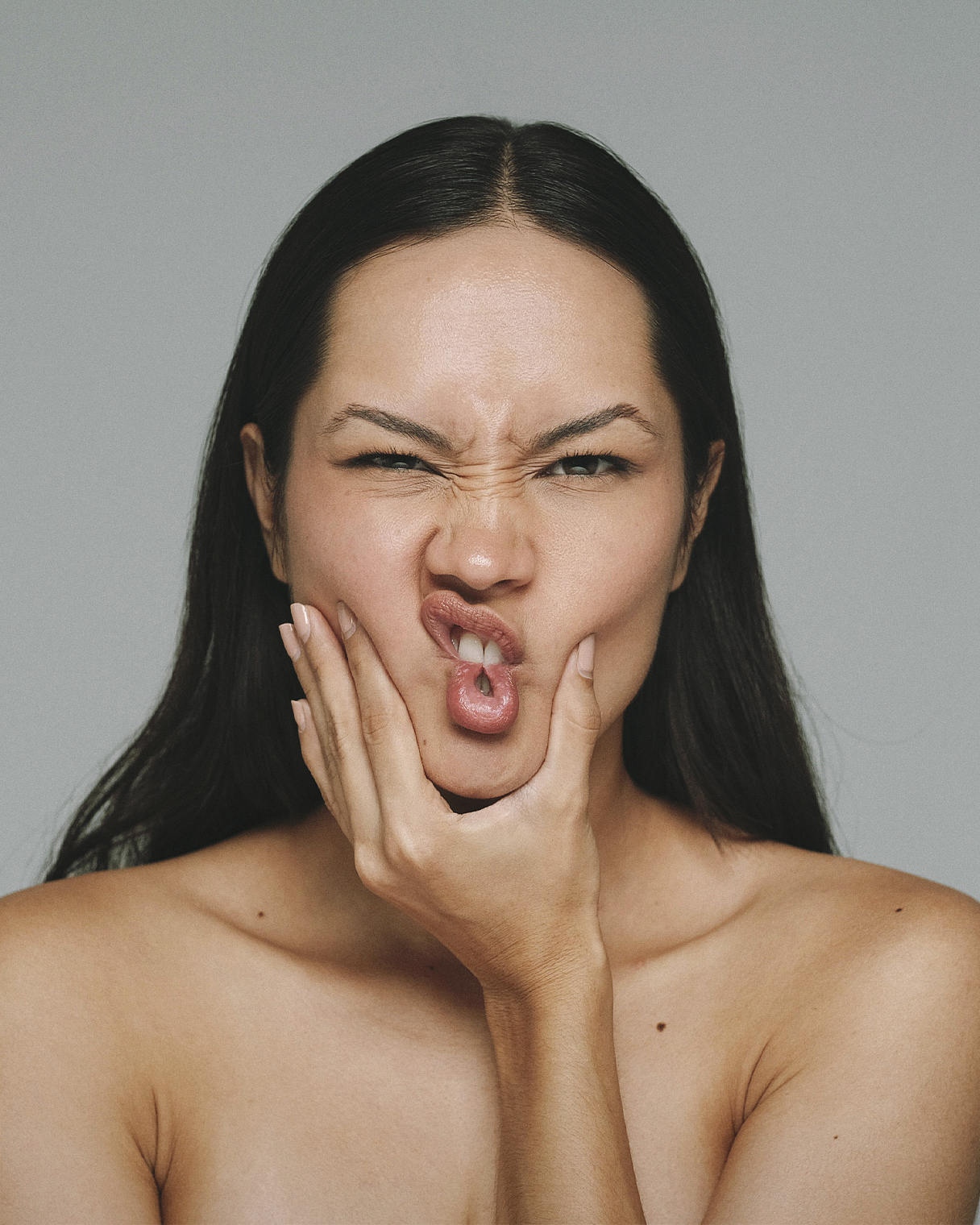 Model squashing her own cheeks and pulling a face in a high-contrast beauty portrait