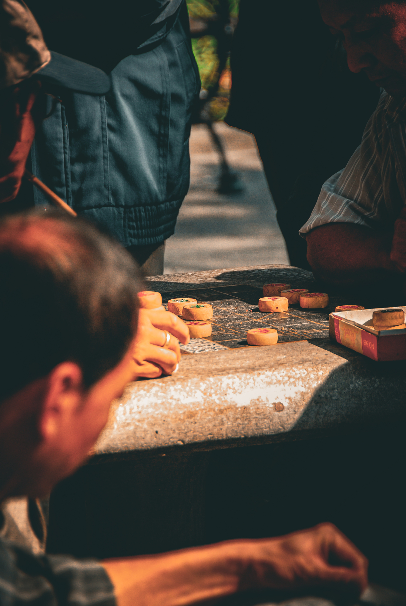 Men bent over a game of Chinese chess on a stone table in warm afternoon light