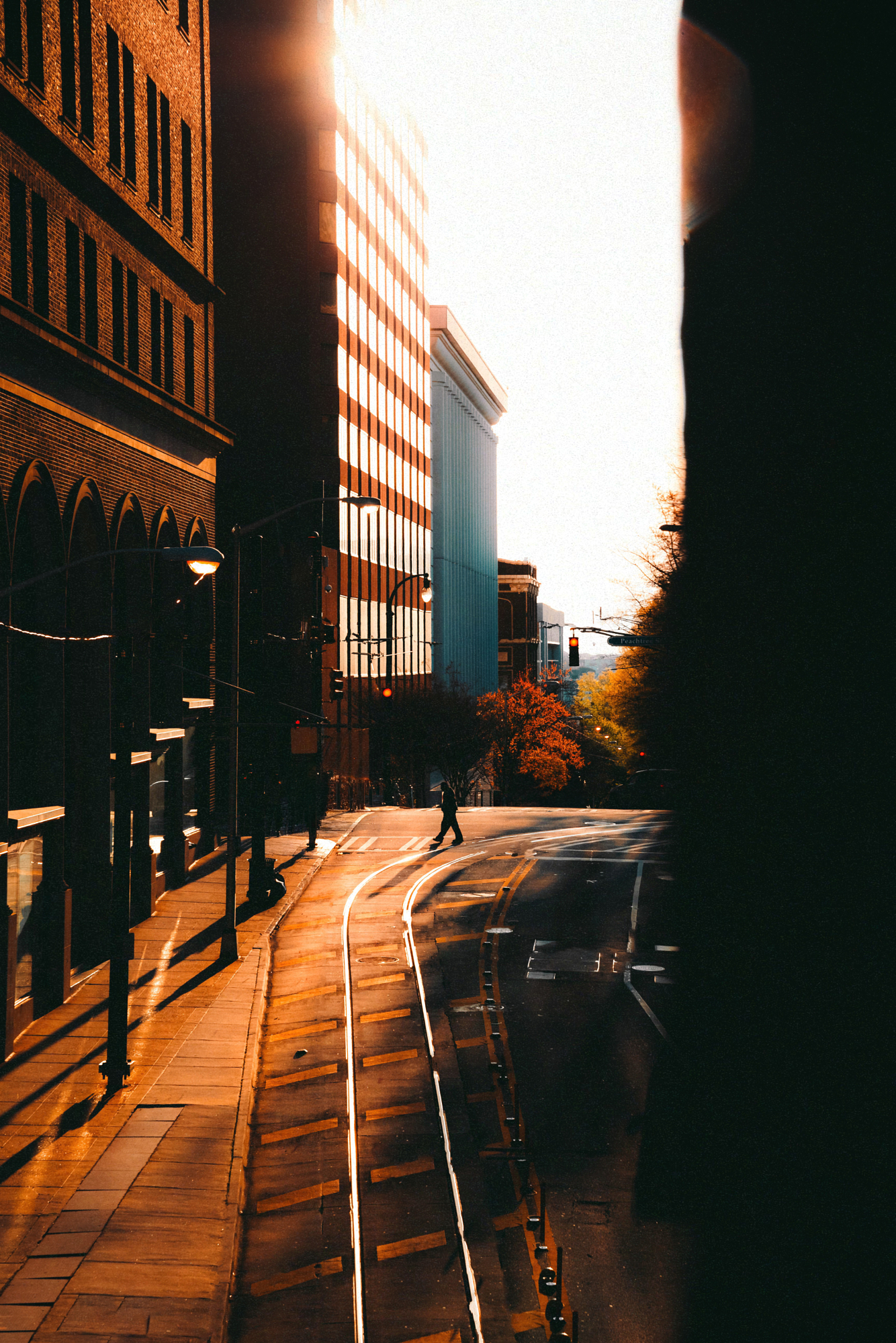 Golden hour light raking down a city street, warm reflected tones bouncing off brick and pavement onto a lone pedestrian