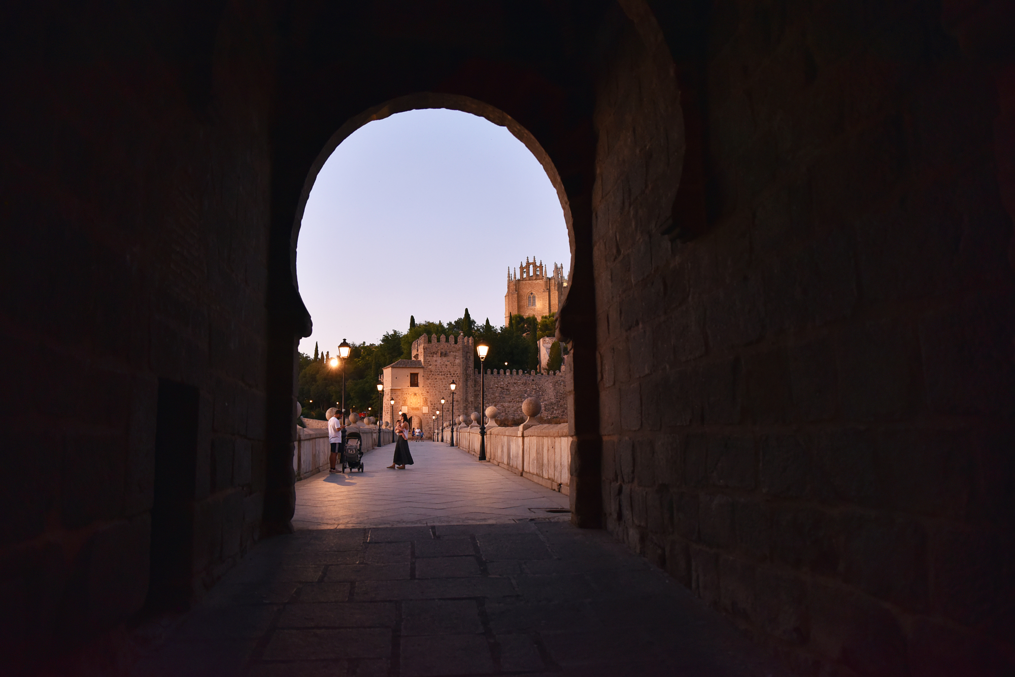 Historic stone archway framing a bridge and lit castle in Toledo Spain at dusk, photographer Gonzalo Bendito