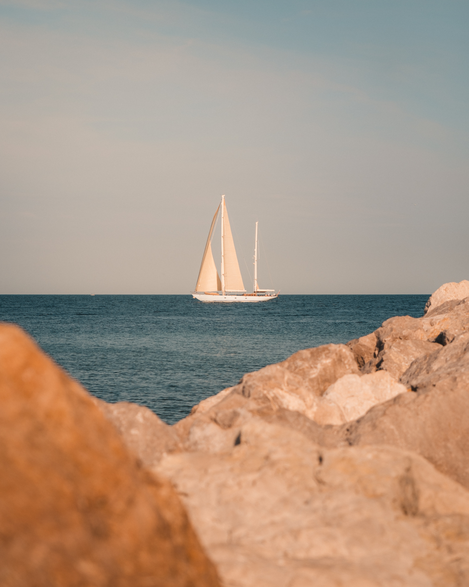 Sailboat drifting on the horizon, framed between sunlit coastal rocks
