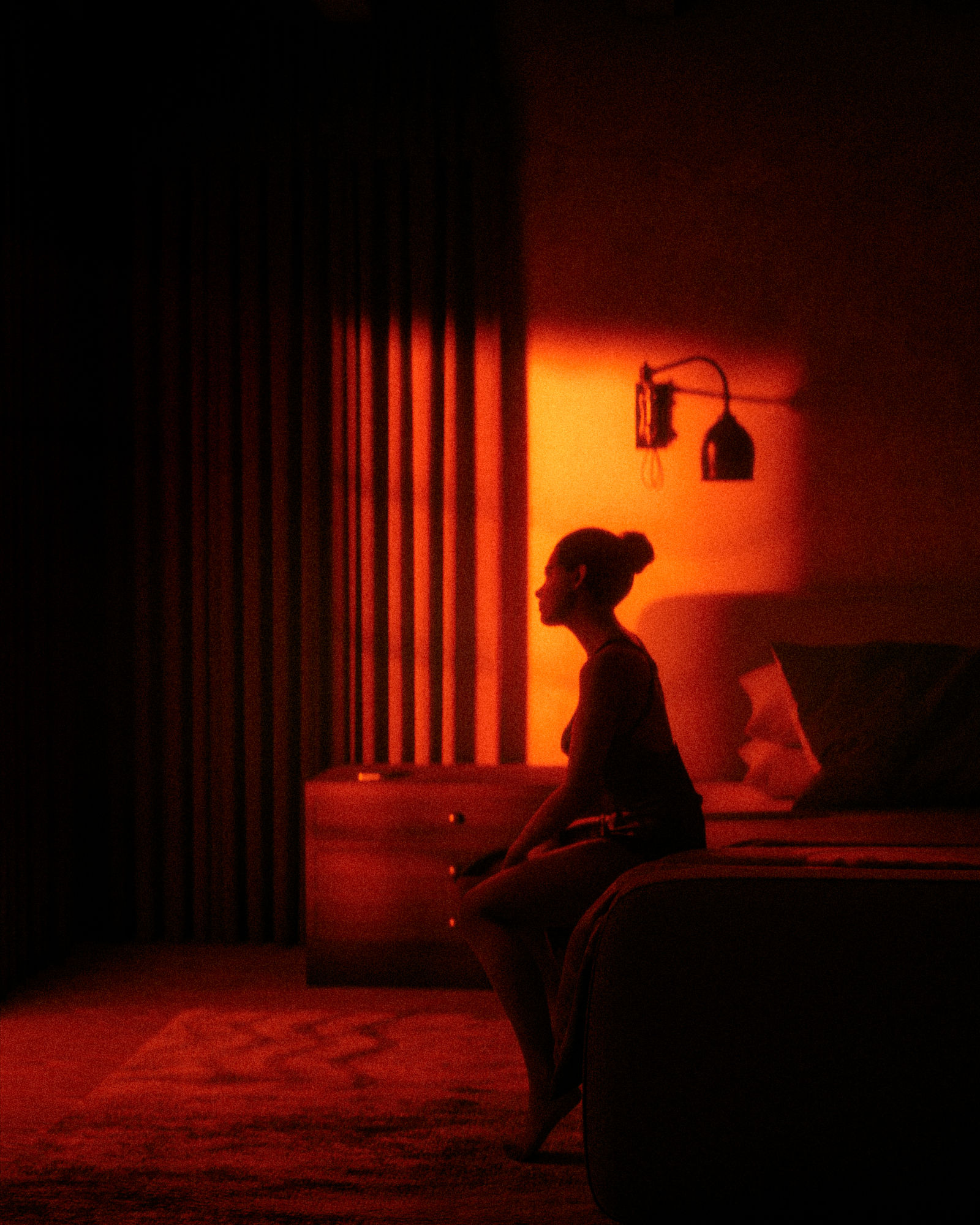 Woman silhouetted in a dark room against a wall washed in warm amber lamp light, a low Kelvin natural light photography scene