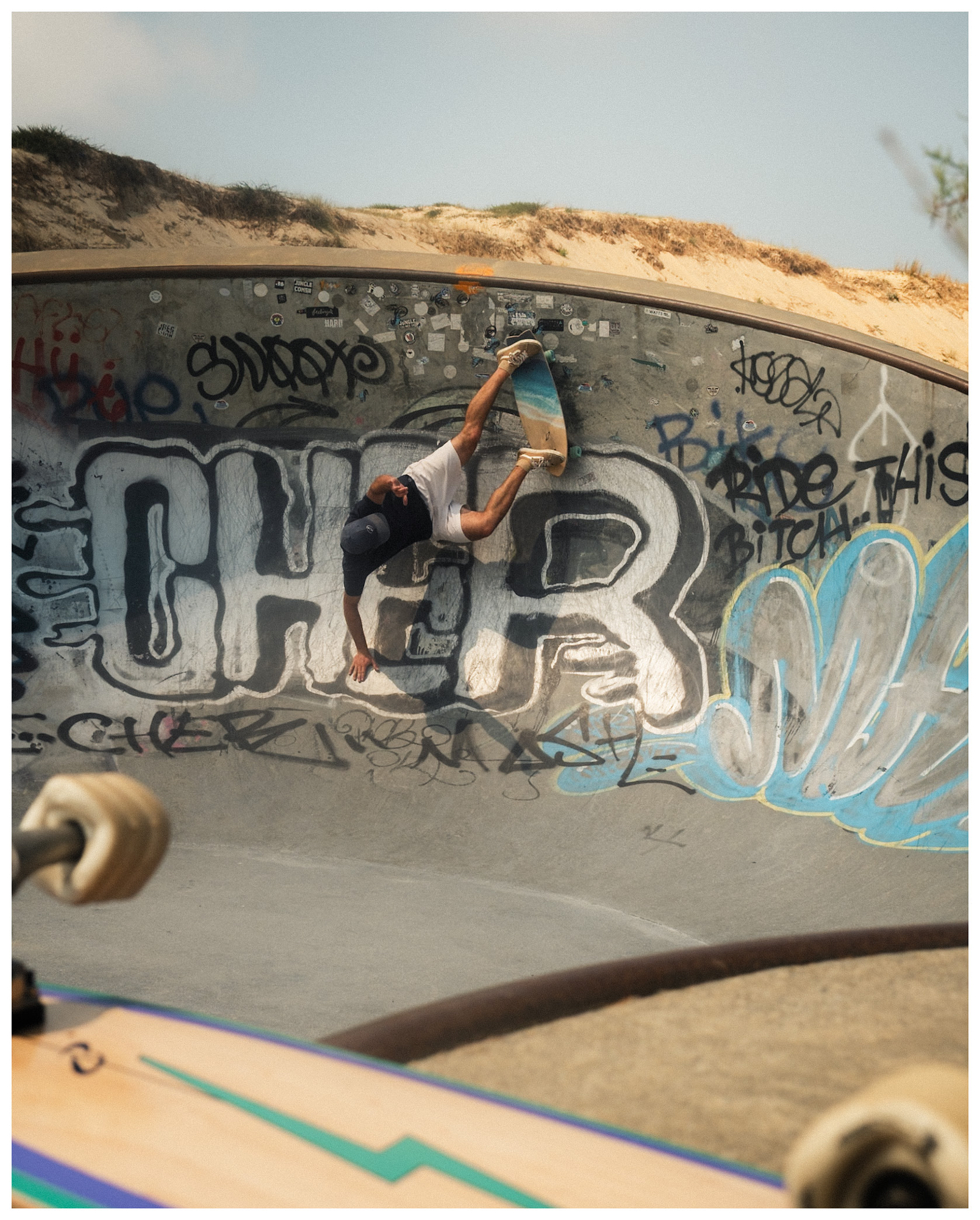 Skateboarder carving a graffiti-covered concrete bowl beside coastal sand dunes