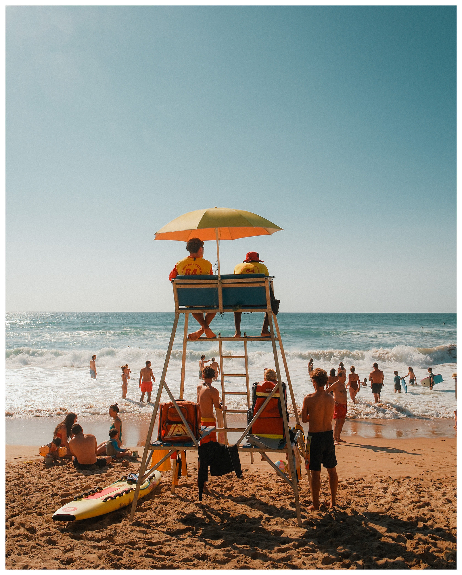 Lifeguards watching swimmers from a wooden tower under an orange beach umbrella.