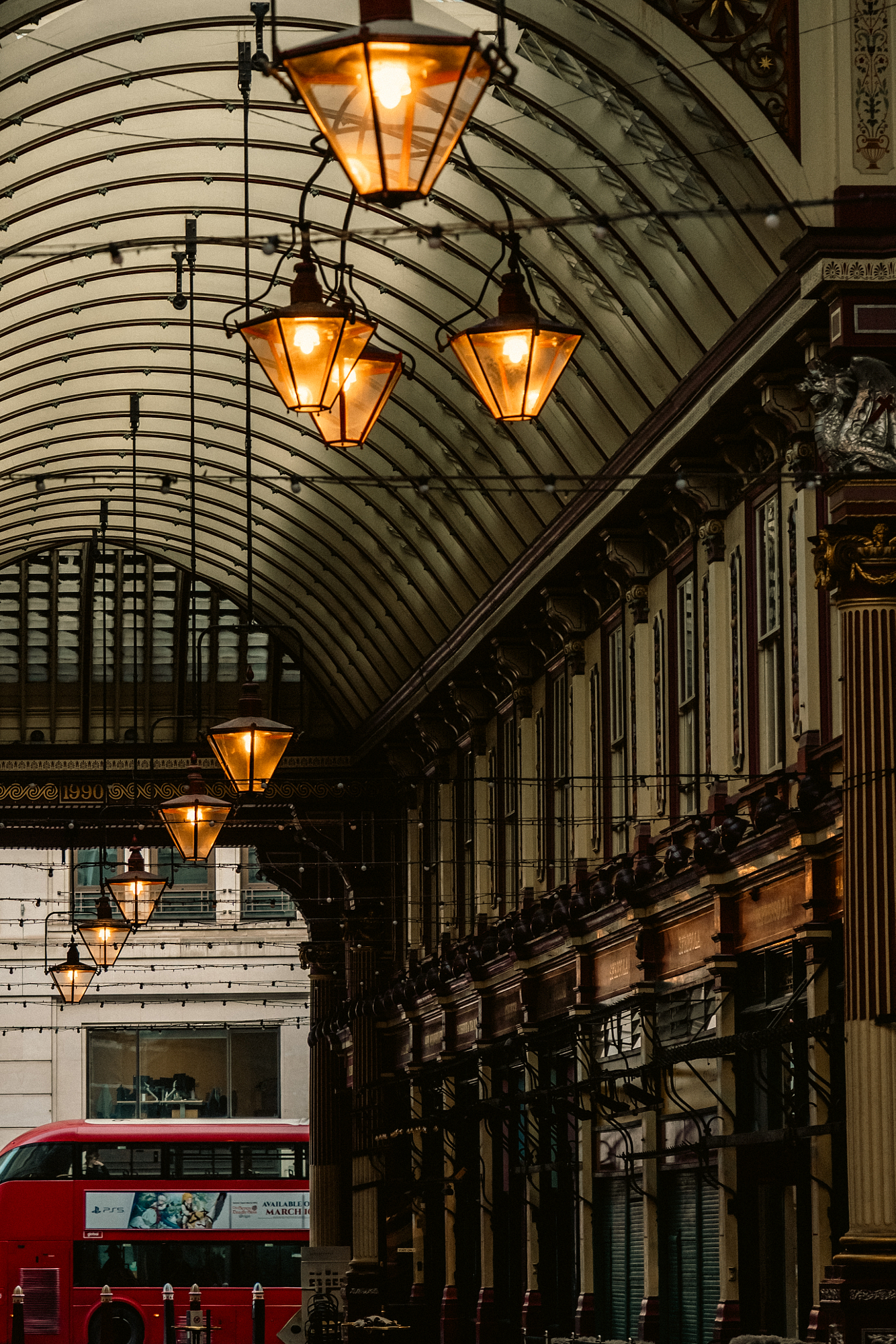 Lanterns hanging under the arched roof of Leadenhall Market with a red London bus below