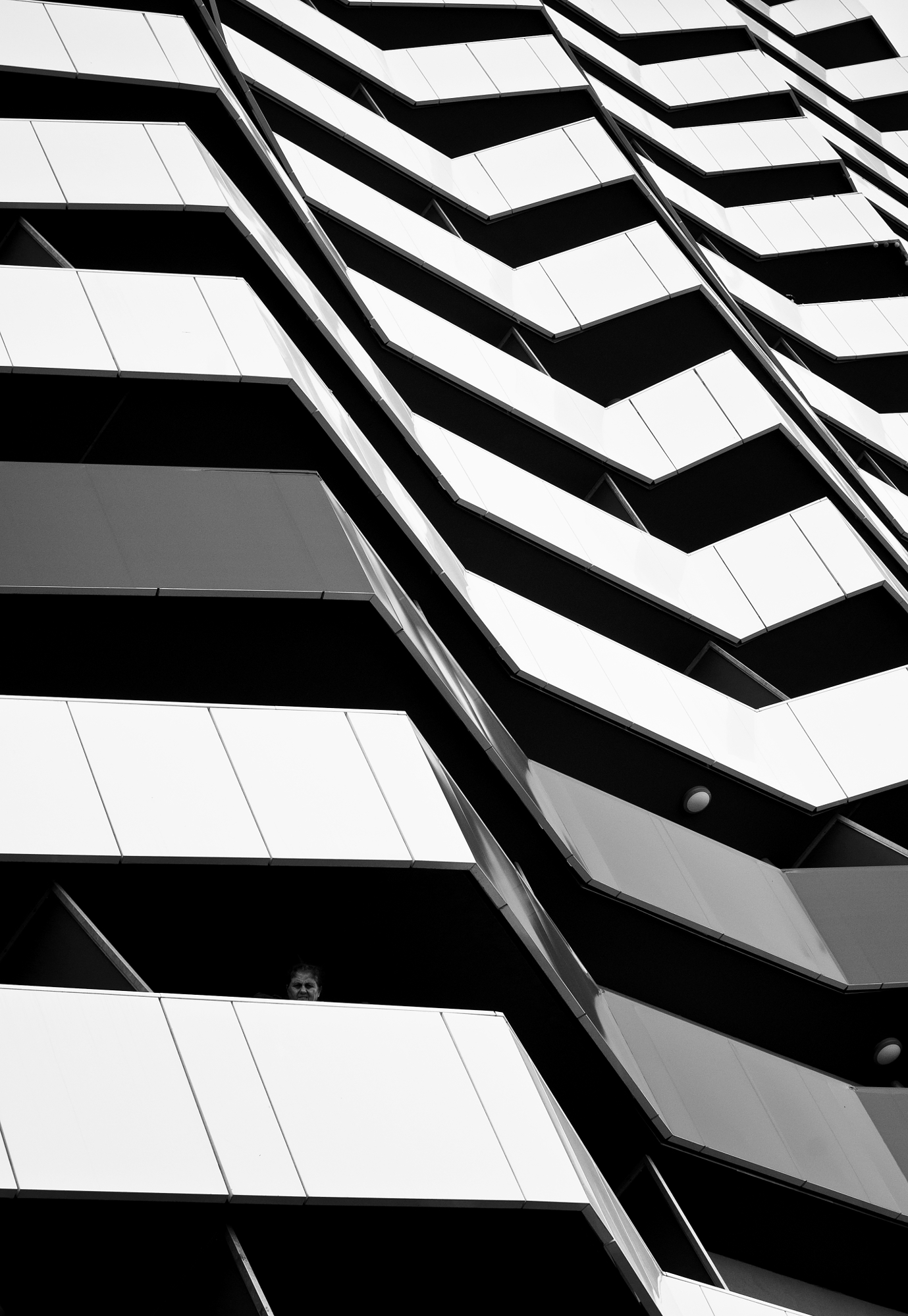 Angular black and white balconies with a single face visible in one window