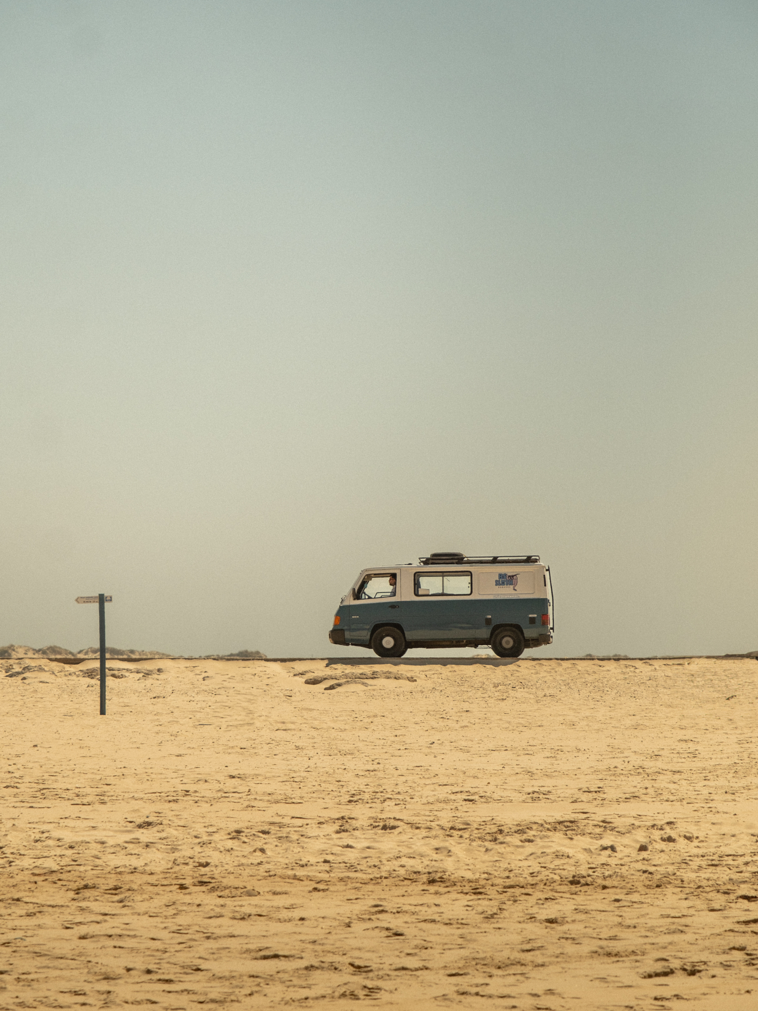 Vintage camper van parked on an empty stretch of sand under a pale sky.