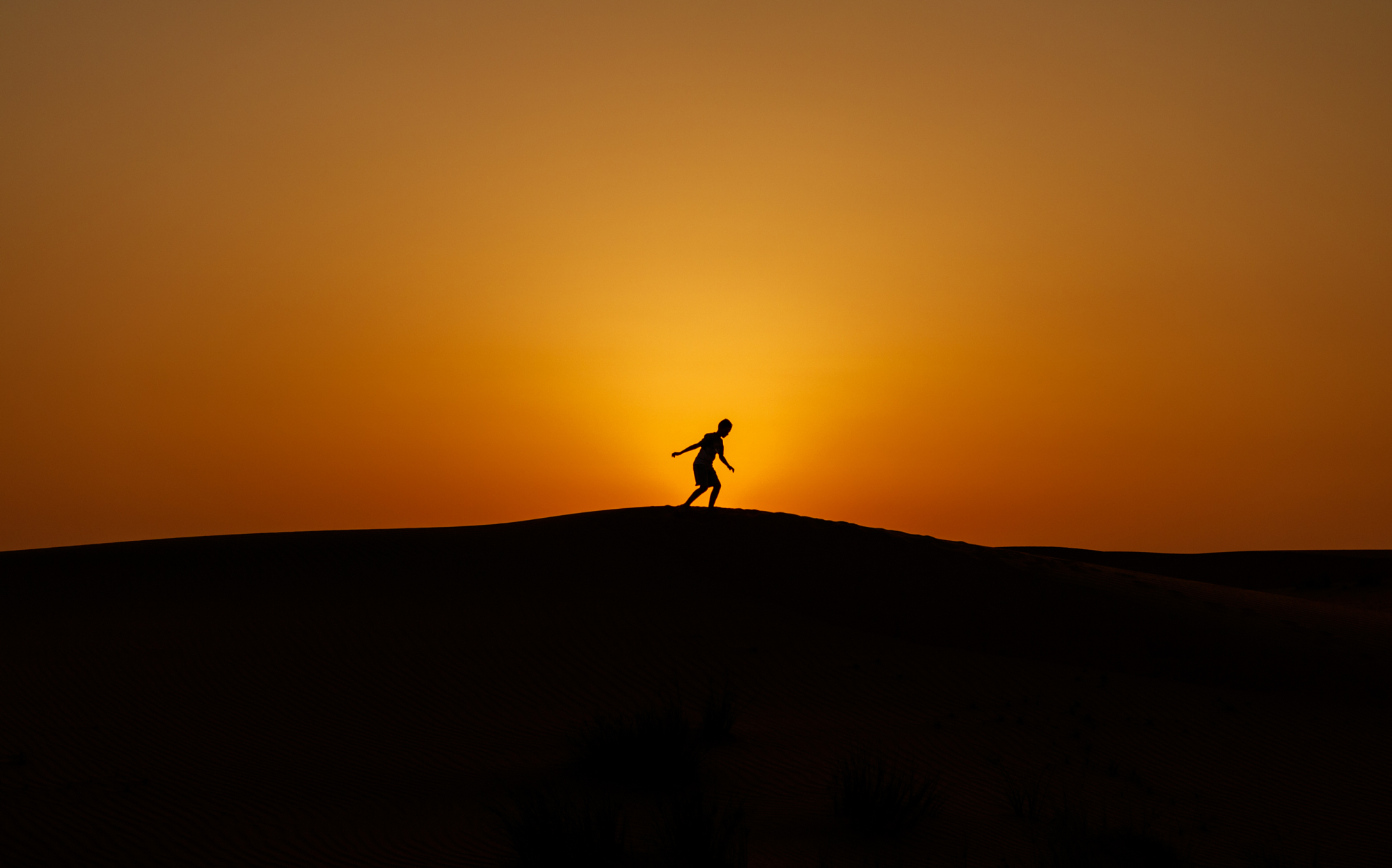 Silhouette of a person running across a desert dune ridge against a glowing golden hour photography sunset.
