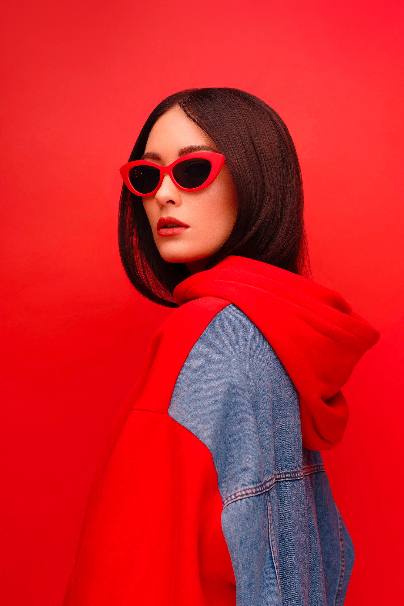 Model in red cat-eye sunglasses and hoodie against a red backdrop, showing high-contrast red color composition.