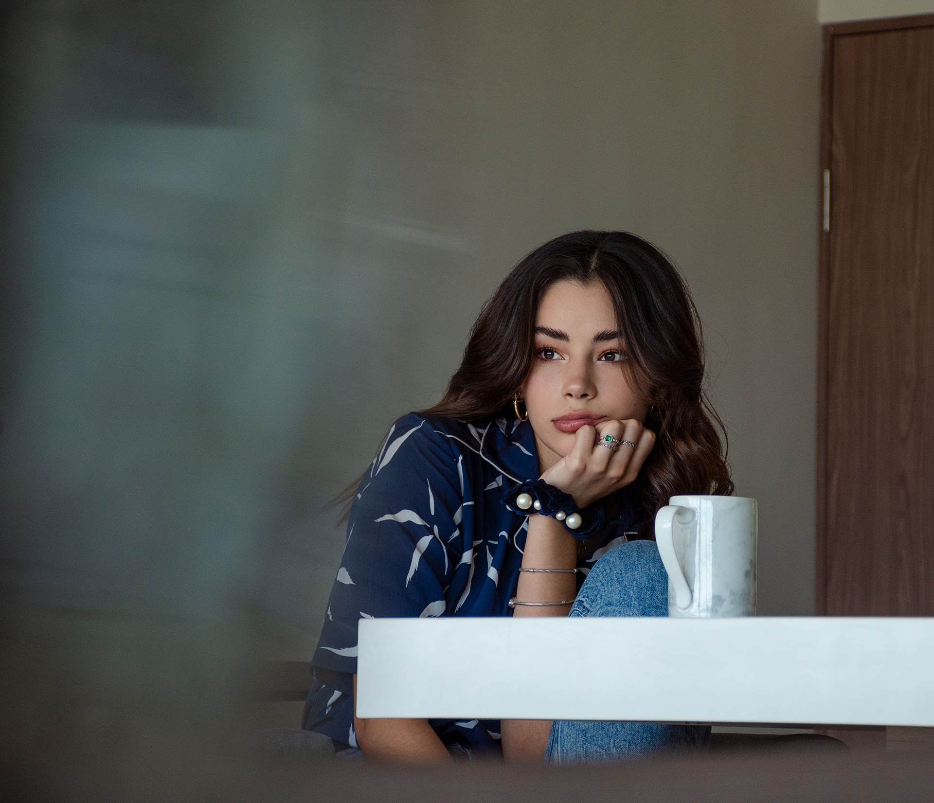 Young woman resting her chin on her hand beside a coffee mug in soft window light