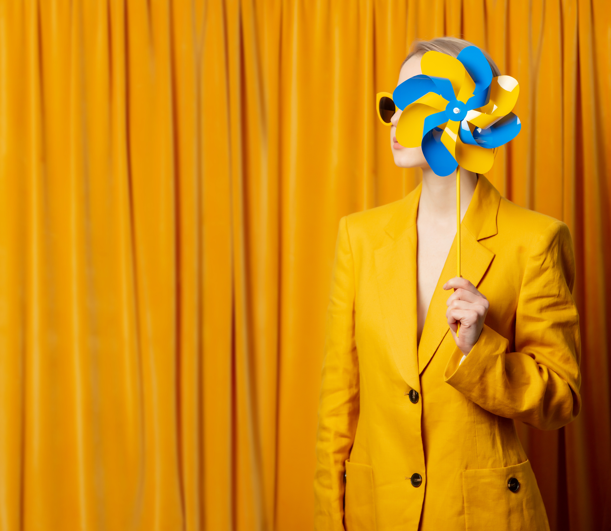 Woman in a yellow blazer holds a blue and yellow pinwheel against an orange curtain, by Vladimir Nikulin Masson.