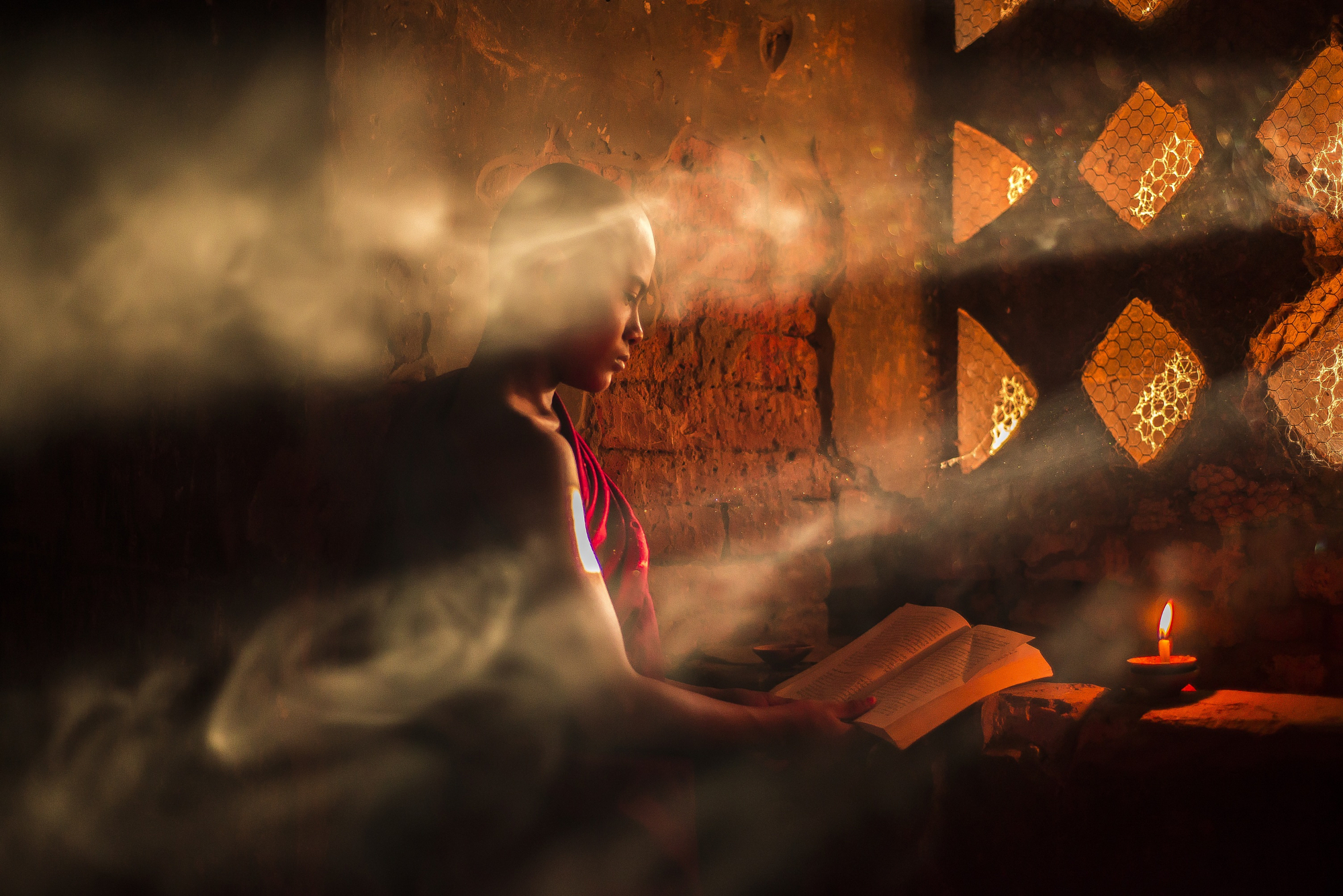 Profile shot of a novice monk reading holy texts by candlelight in a sunlit temple room, photographer Gonzalo Bendito