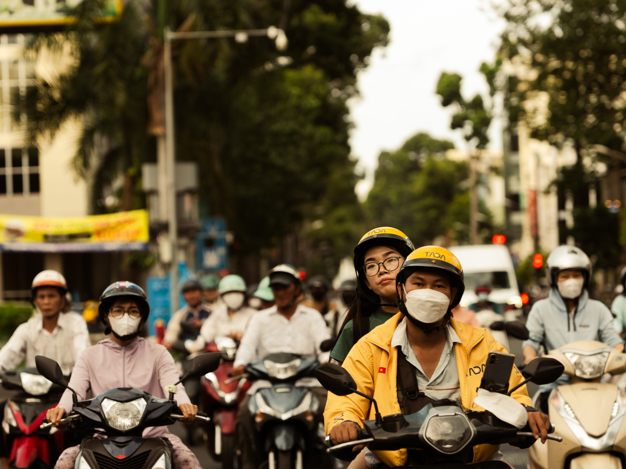 Scooter riders in helmets and face masks waiting at a junction in Vietnam