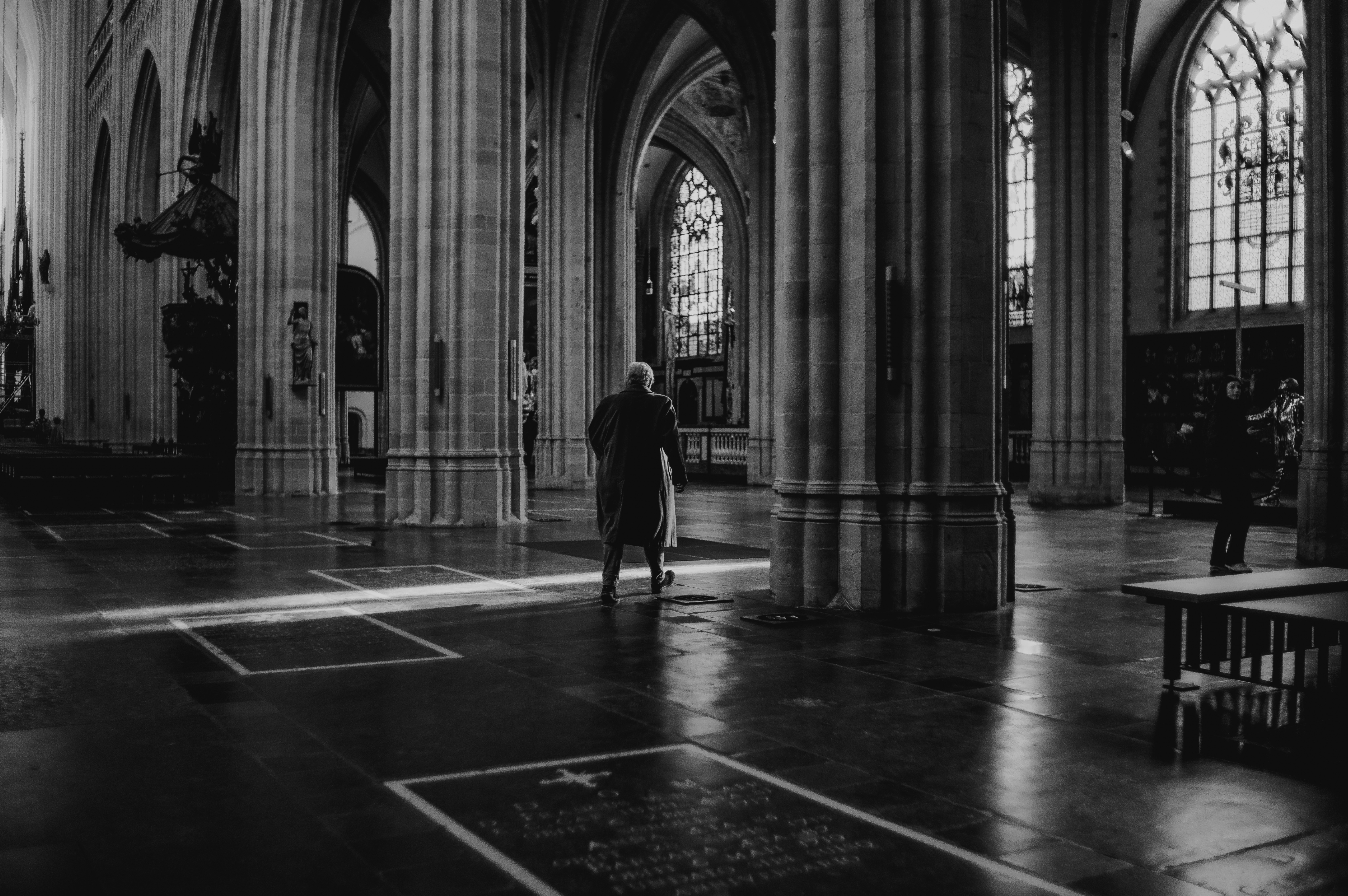 Man in a long coat crossing a shaft of light inside Antwerp cathedral, from Eline Deckers's black and white street photography.