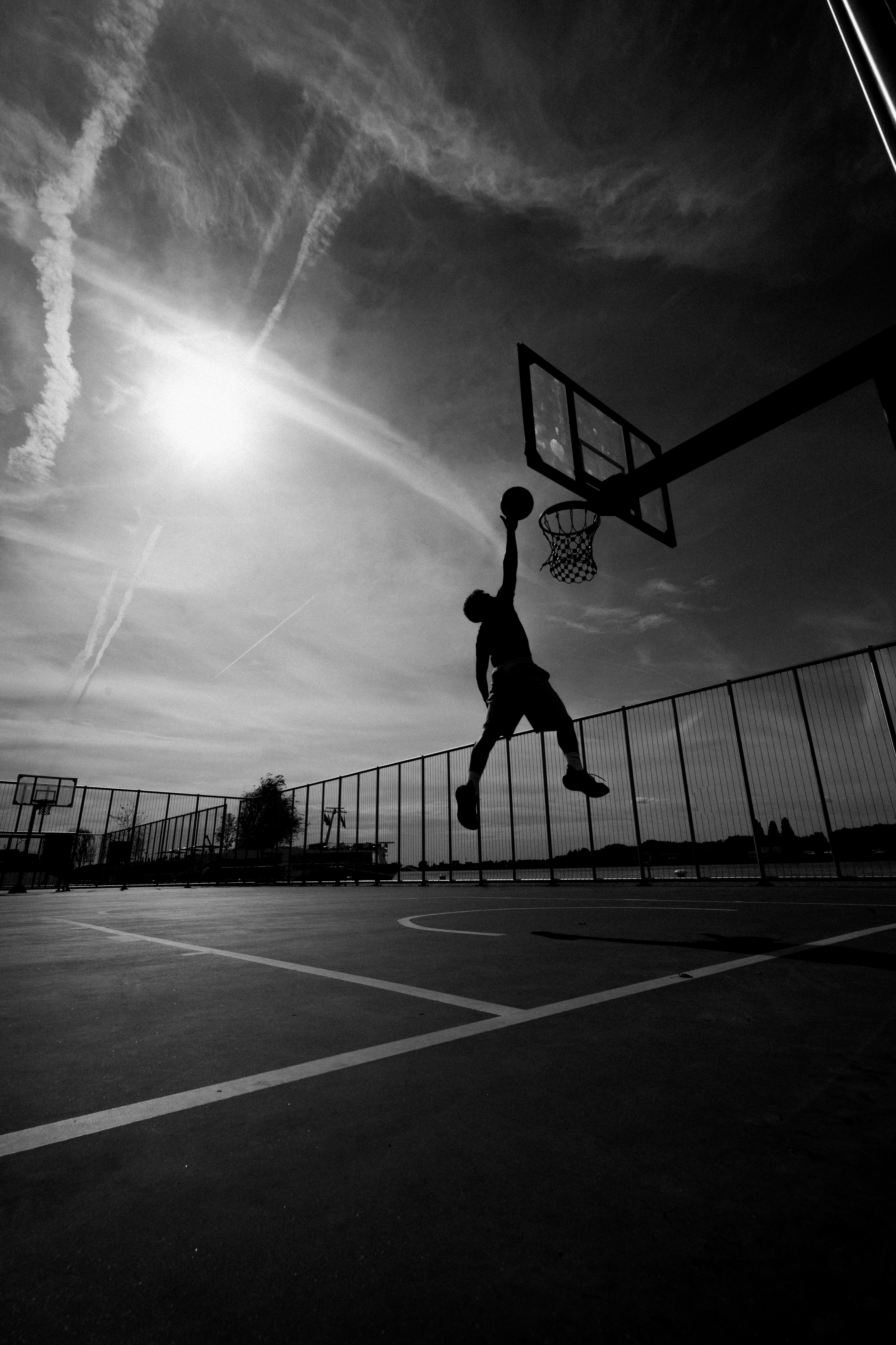 Silhouetted player rising to dunk against the sun on an outdoor court, from Eline Deckers's high-contrast street photography.