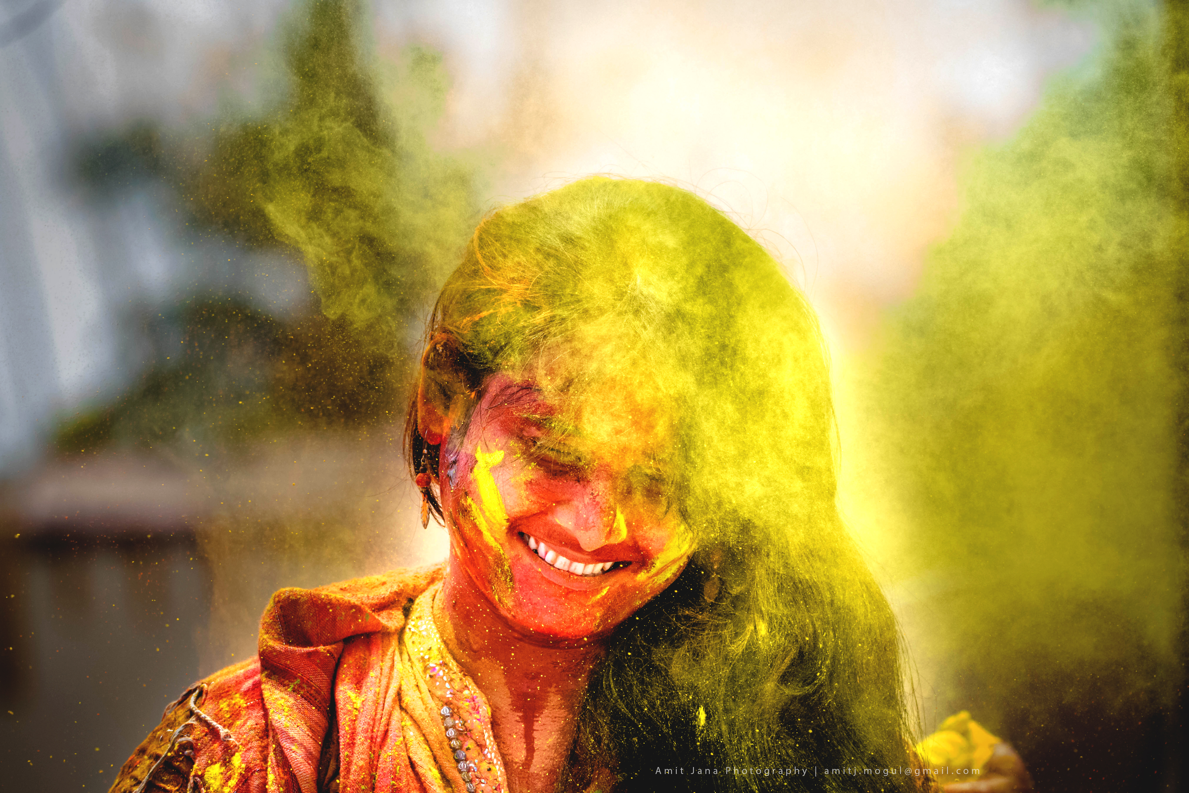 Smiling woman covered in yellow and red Holi powder, high saturation color photography conveying immediacy and joy.