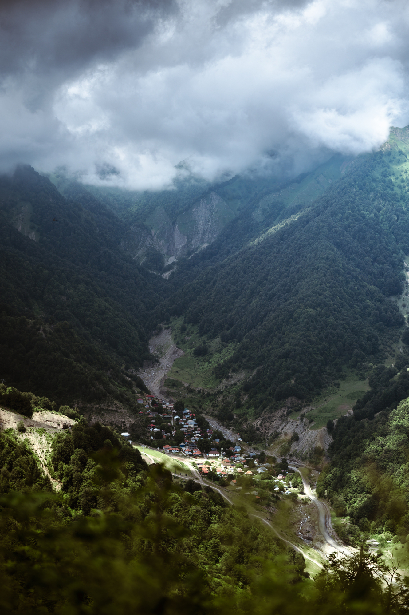 Village on a valley floor beneath cloud-covered Caucasus peaks, from Andrew Shenouda's travel photography in Azerbaijan.