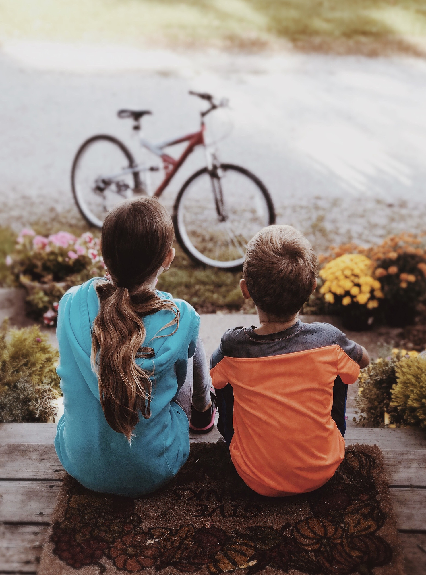 Two children sit close together on porch steps facing a bike, a candid moment of real human connection photography.
