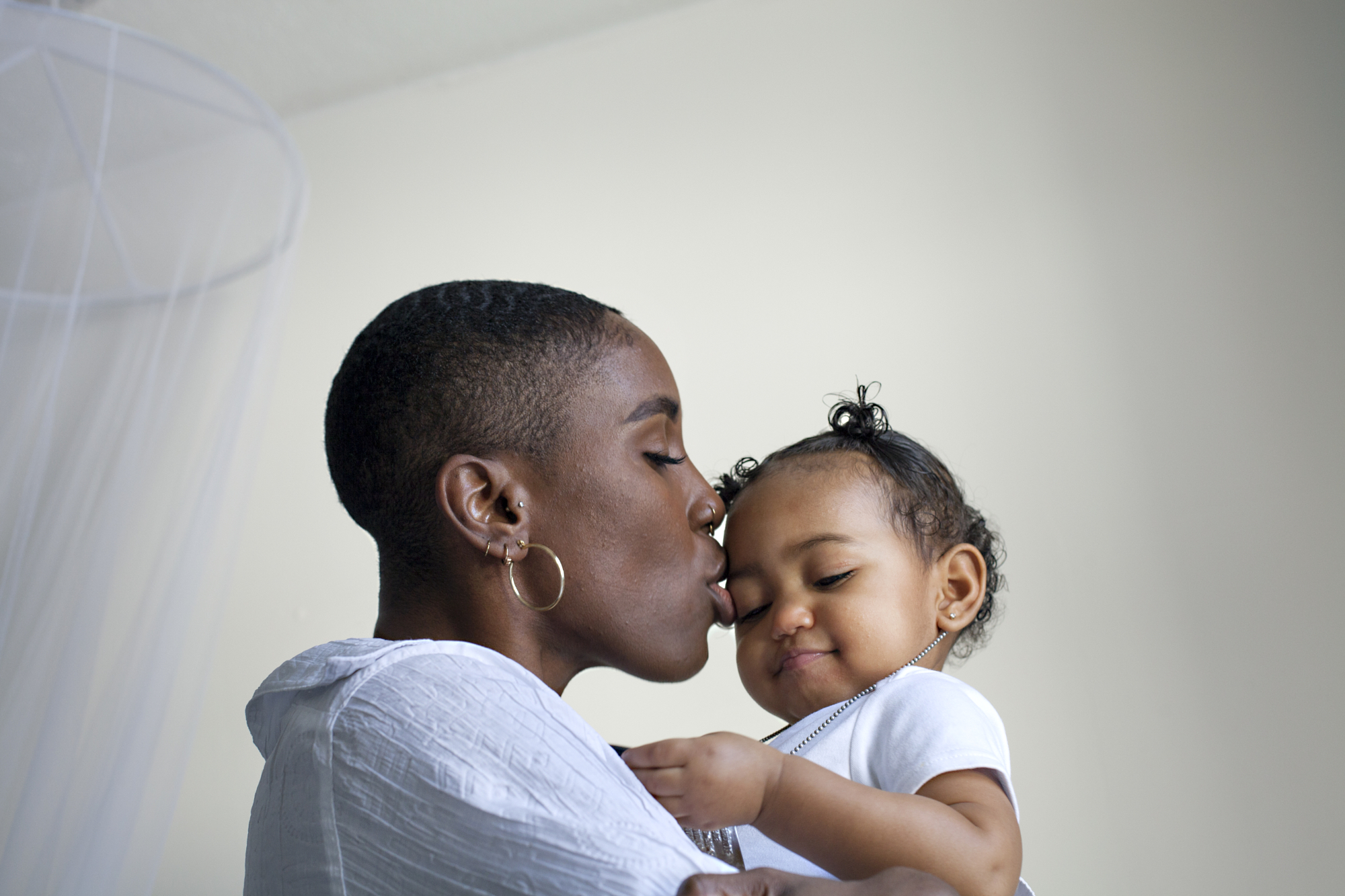 Mother kisses her toddler on the forehead as the child smiles, an emotional photography moment between parent and child.