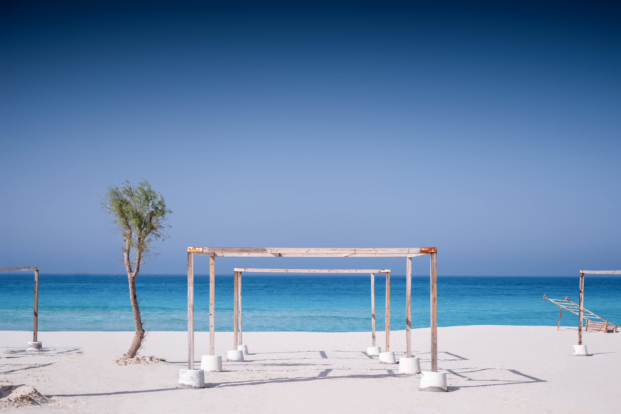 Bare timber beach pergolas on white sand facing turquoise water, a minimalist frame from Andrew Shenouda's photography on Egypt's North Coast.
